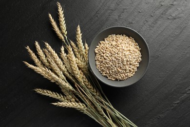 Photo of Many wheat spikes and grains on black table, flat lay
