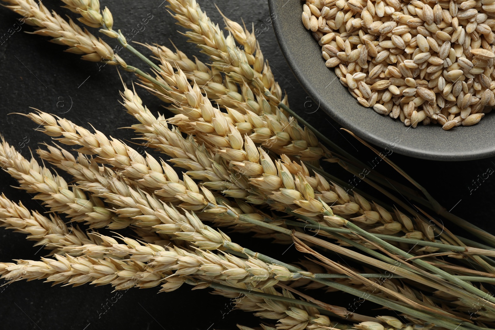 Photo of Many wheat spikes and grains on black table, flat lay