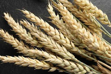 Photo of Many wheat spikes on black table, top view