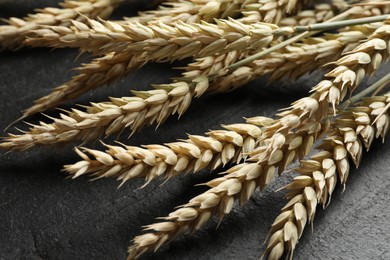 Photo of Many wheat spikes on black table, closeup