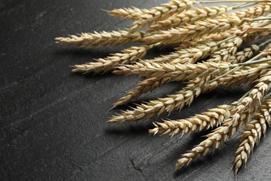 Photo of Many wheat spikes on black table, closeup. Space for text