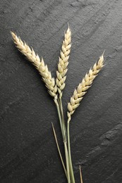 Photo of Wheat spikes on black table, flat lay
