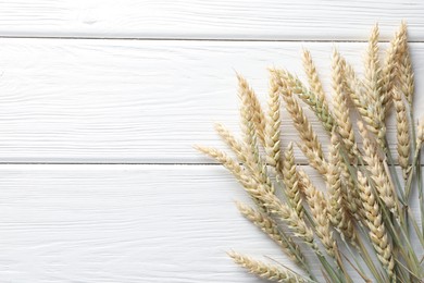 Photo of Many wheat spikes on white wooden table, flat lay. Space for text