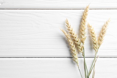 Photo of Many wheat spikes on white wooden table, flat lay. Space for text