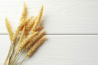 Photo of Many wheat spikes on white wooden table, flat lay. Space for text