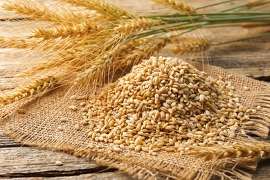 Photo of Wheat spikes and grains on wooden table, closeup
