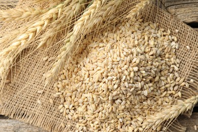 Photo of Wheat spikes and grains on wooden table, top view