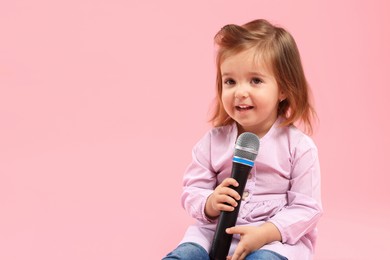 Photo of Cute little girl with microphone on pink background, space for text