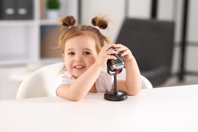 Photo of Cute little girl with microphone on at white table indoors