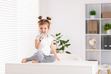 Photo of Cute little girl with microphone on white table at home, space for text