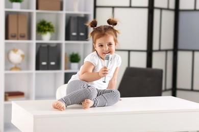 Photo of Cute little girl with microphone on white table at home