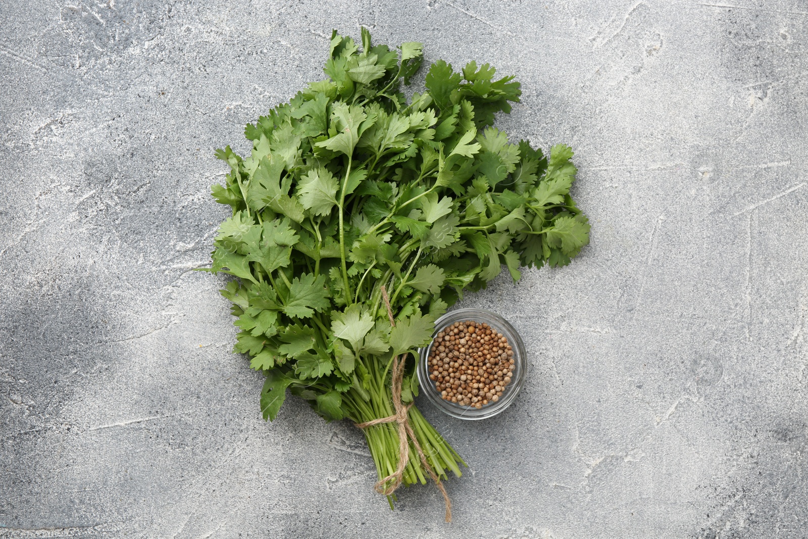 Photo of Fresh cilantro leaf and coriander seeds on grey table, top view