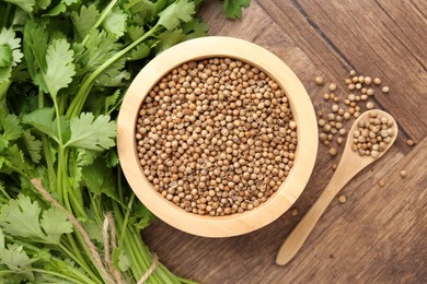 Photo of Fresh cilantro and coriander seeds on wooden table, top view