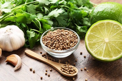 Photo of Fresh cilantro, coriander seeds, lime and garlic on wooden table, closeup