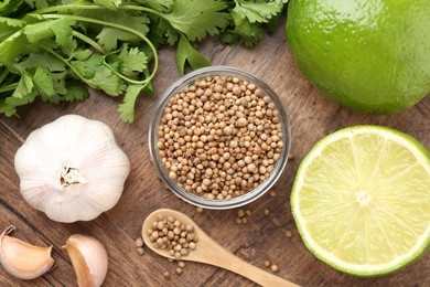 Photo of Fresh cilantro, coriander seeds, lime and garlic on wooden table, flat lay