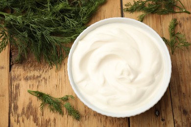 Photo of Tasty sour cream in bowl and dill on wooden table, flat lay