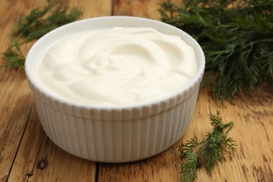 Photo of Tasty sour cream in bowl and dill on wooden table, closeup