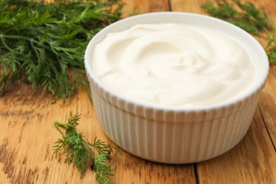 Photo of Tasty sour cream in bowl and dill on wooden table, closeup