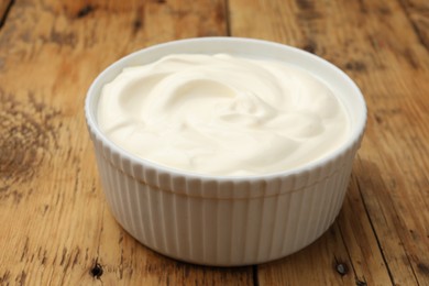 Photo of Tasty sour cream in bowl on wooden table, closeup
