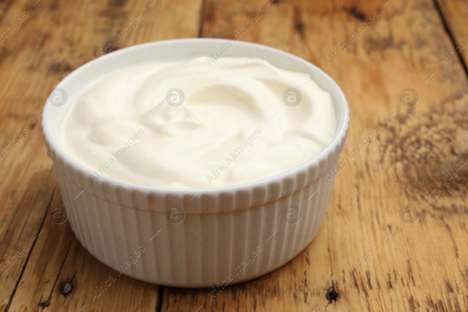 Photo of Tasty sour cream in bowl on wooden table, closeup