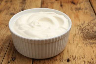 Photo of Tasty sour cream in bowl on wooden table, closeup