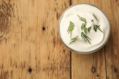 Photo of Tasty sour cream in bowl and dill on wooden table, top view. Space for text