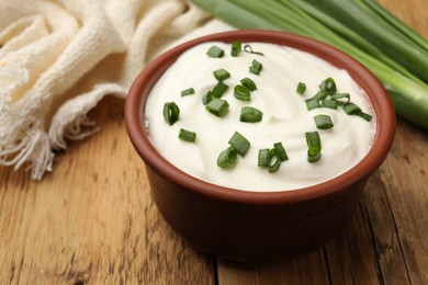 Photo of Tasty sour cream in bowl and green onions on wooden table, closeup