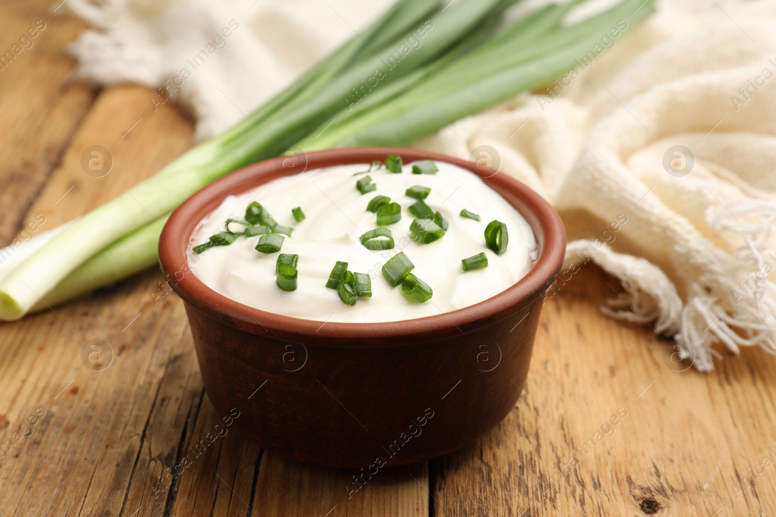 Photo of Tasty sour cream in bowl and green onions on wooden table, closeup