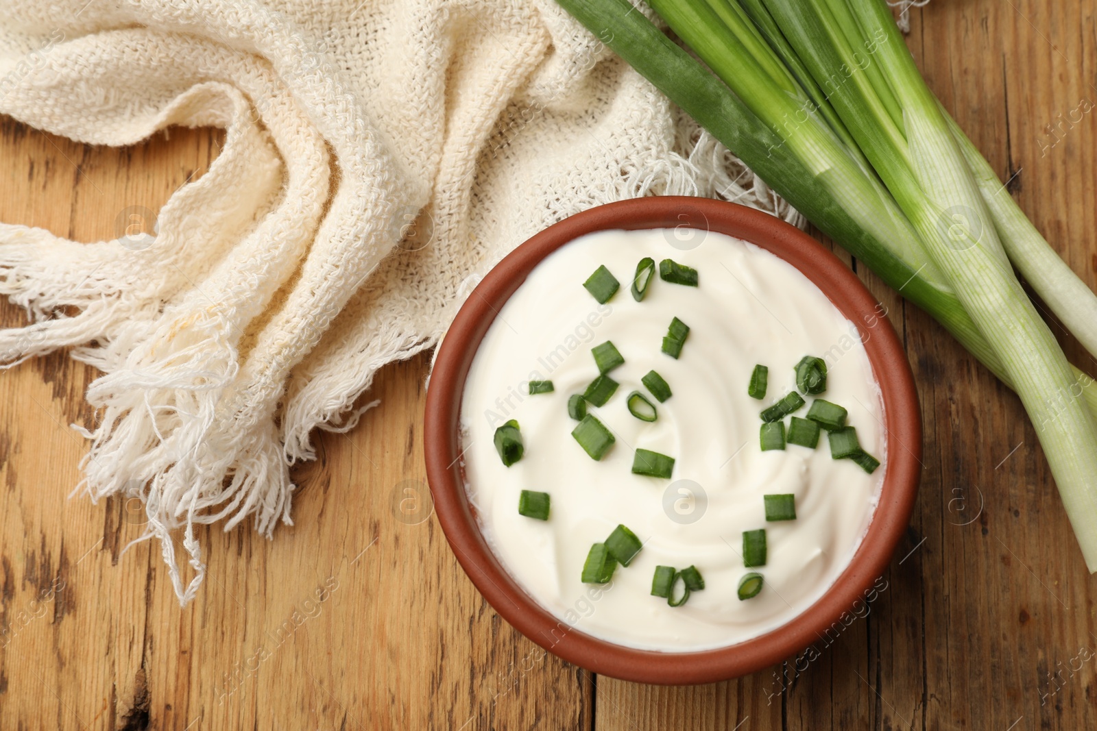 Photo of Tasty sour cream in bowl and green onions on wooden table, flat lay