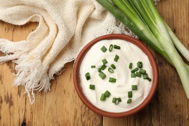 Photo of Tasty sour cream in bowl and green onions on wooden table, flat lay