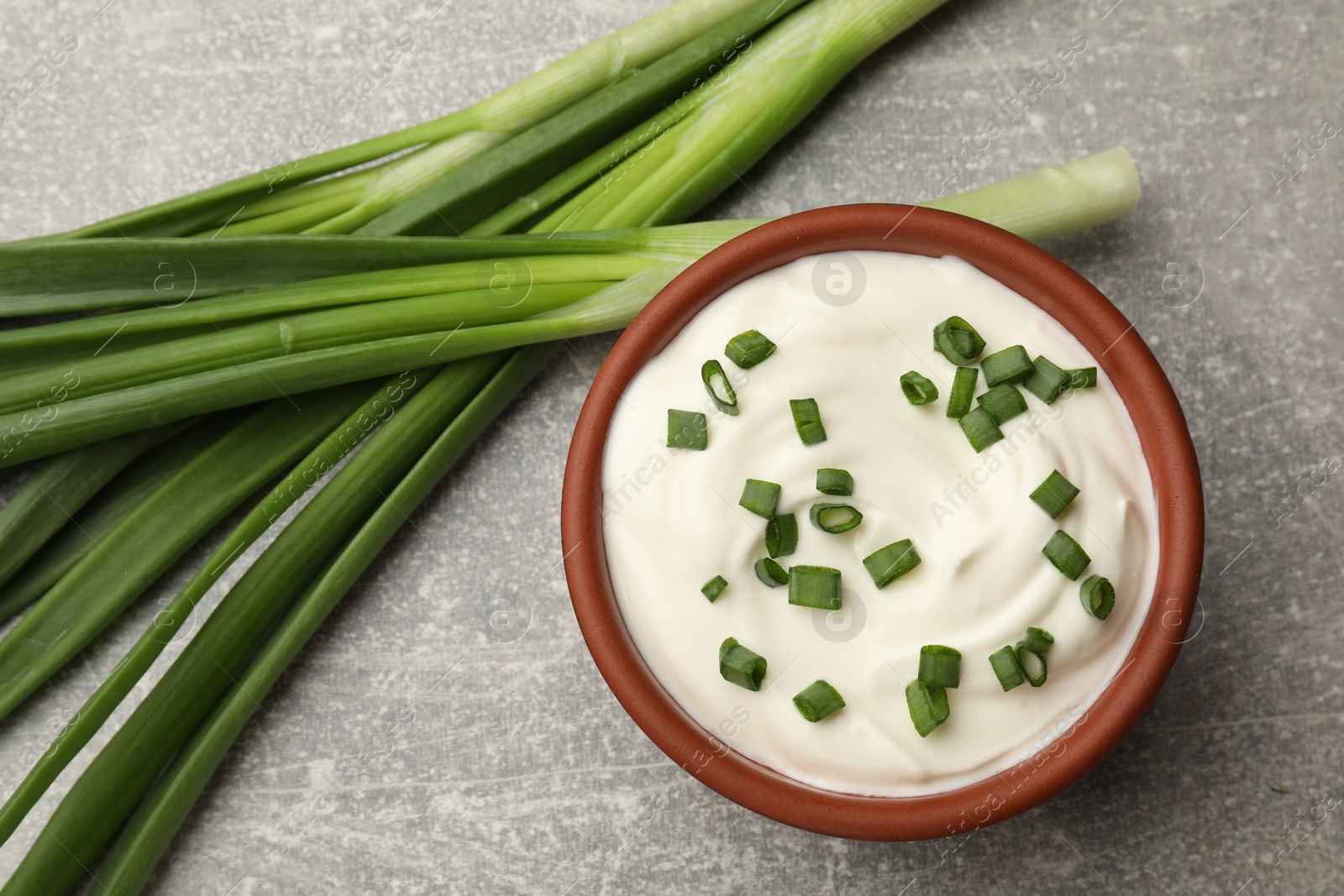 Tasty sour cream in bowl and green onions on grey table, flat lay Photo of Tasty sour cream in bowl and green onions on grey table, flat lay