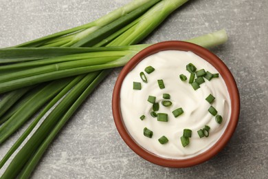 Photo of Tasty sour cream in bowl and green onions on grey table, flat lay