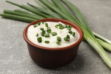 Photo of Tasty sour cream in bowl and green onions on grey table, closeup