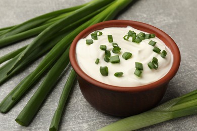 Photo of Tasty sour cream in bowl and green onions on grey table, closeup