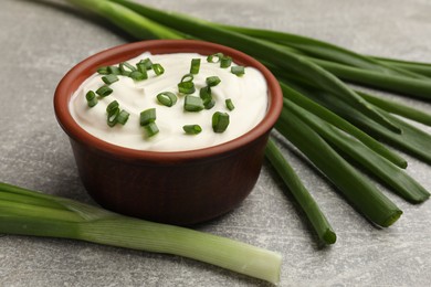 Photo of Tasty sour cream in bowl and green onions on grey table, closeup