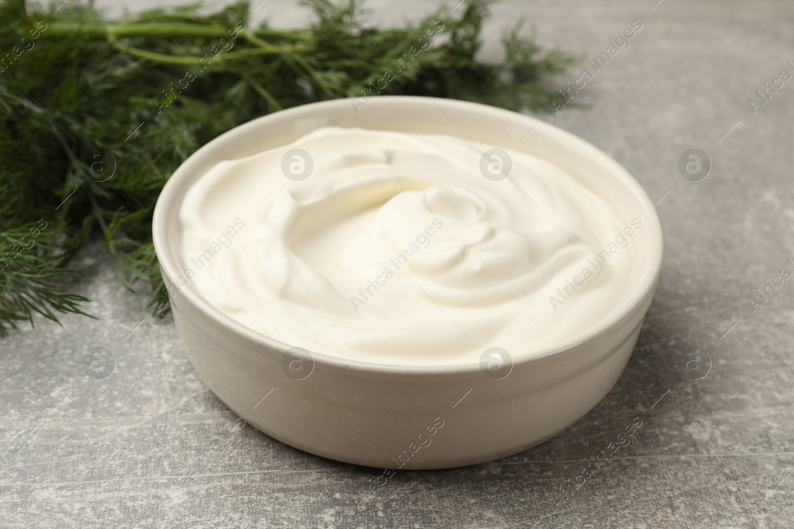 Photo of Tasty sour cream in bowl and dill on grey table, closeup