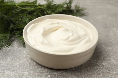 Photo of Tasty sour cream in bowl and dill on grey table, closeup