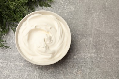 Photo of Tasty sour cream in bowl and dill on grey table, flat lay. Space for text