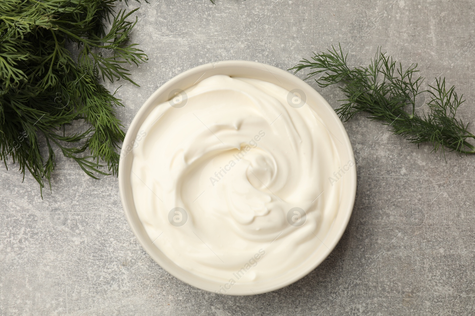 Photo of Tasty sour cream in bowl and dill on grey table, flat lay