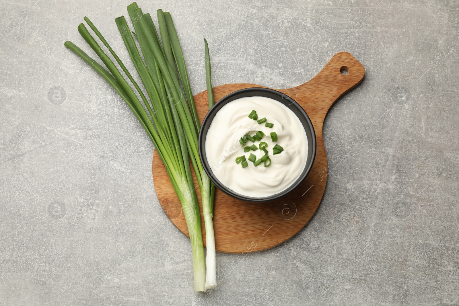 Tasty sour cream in bowl and green onions on grey table, top view Photo of Tasty sour cream in bowl and green onions on grey table, top view