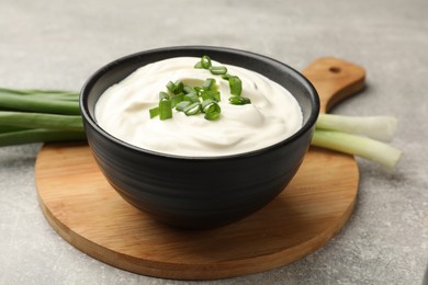 Photo of Tasty sour cream in bowl and green onions on grey table, closeup