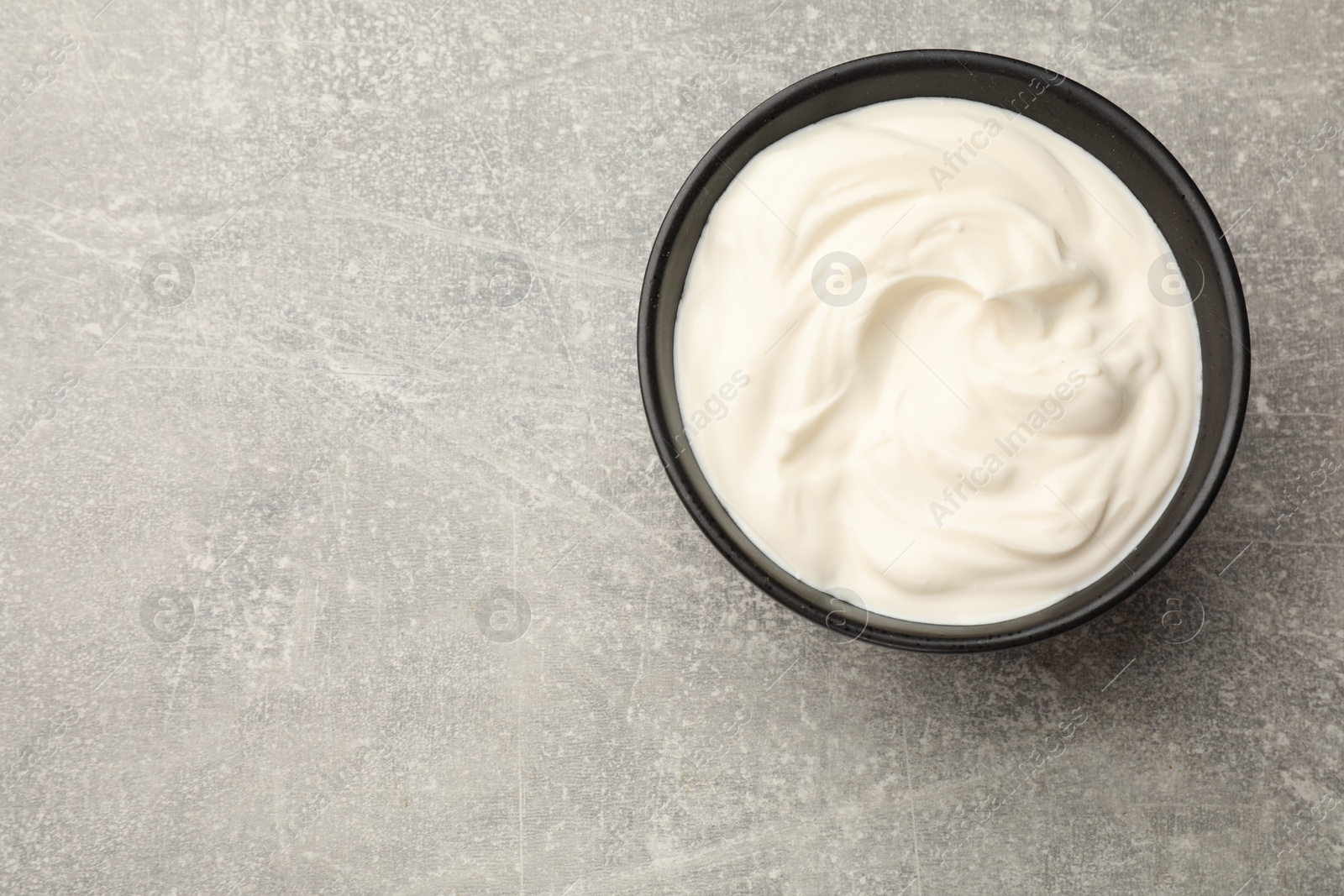 Photo of Tasty sour cream in bowl on grey table, top view. Space for text