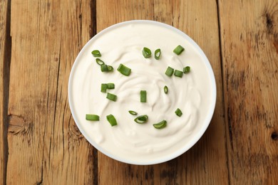 Photo of Tasty sour cream with green onions in bowl on wooden table, top view