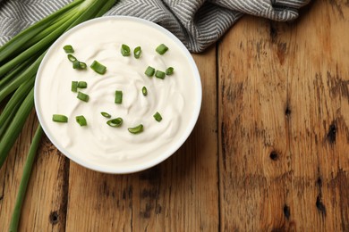 Photo of Tasty sour cream in bowl and green onions on wooden table, flat lay. Space for text