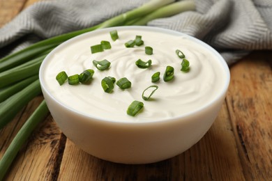Photo of Tasty sour cream in bowl and green onions on wooden table, closeup
