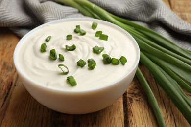 Photo of Tasty sour cream in bowl and green onions on wooden table, closeup