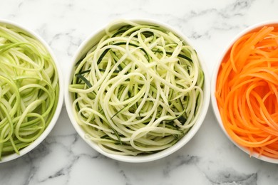 Photo of Different vegetable noodles in bowls on white marble table, flat lay. Vegetarian dish