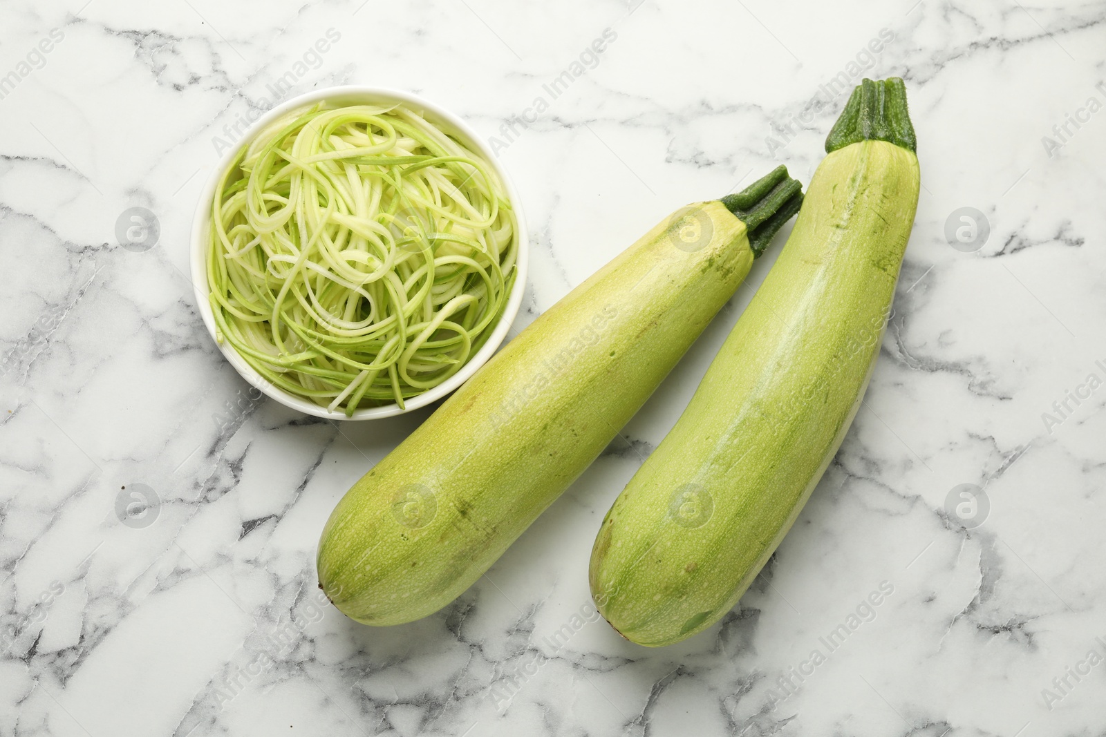 Raw squash noodles and fresh vegetables on white marble table, flat lay. Vegetarian dish Photo of Raw squash noodles and fresh vegetables on white marble table, flat lay. Vegetarian dish