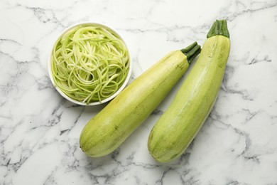 Photo of Raw squash noodles and fresh vegetables on white marble table, flat lay. Vegetarian dish