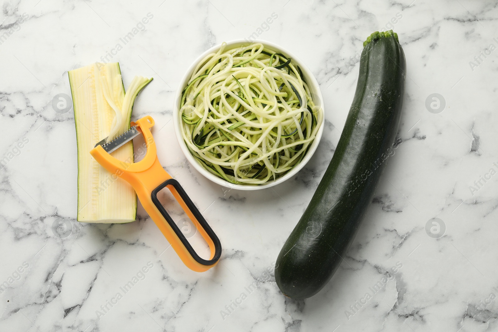 Raw zucchini noodles, peeler and fresh vegetables on white marble table, flat lay. Vegetarian dish Photo of Raw zucchini noodles, peeler and fresh vegetables on white marble table, flat lay. Vegetarian dish